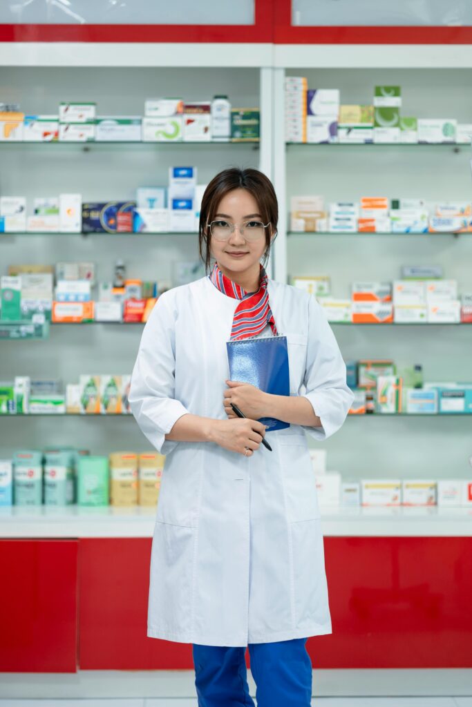 Female pharmacist in a lab coat standing confidently in a well-organized pharmacy.